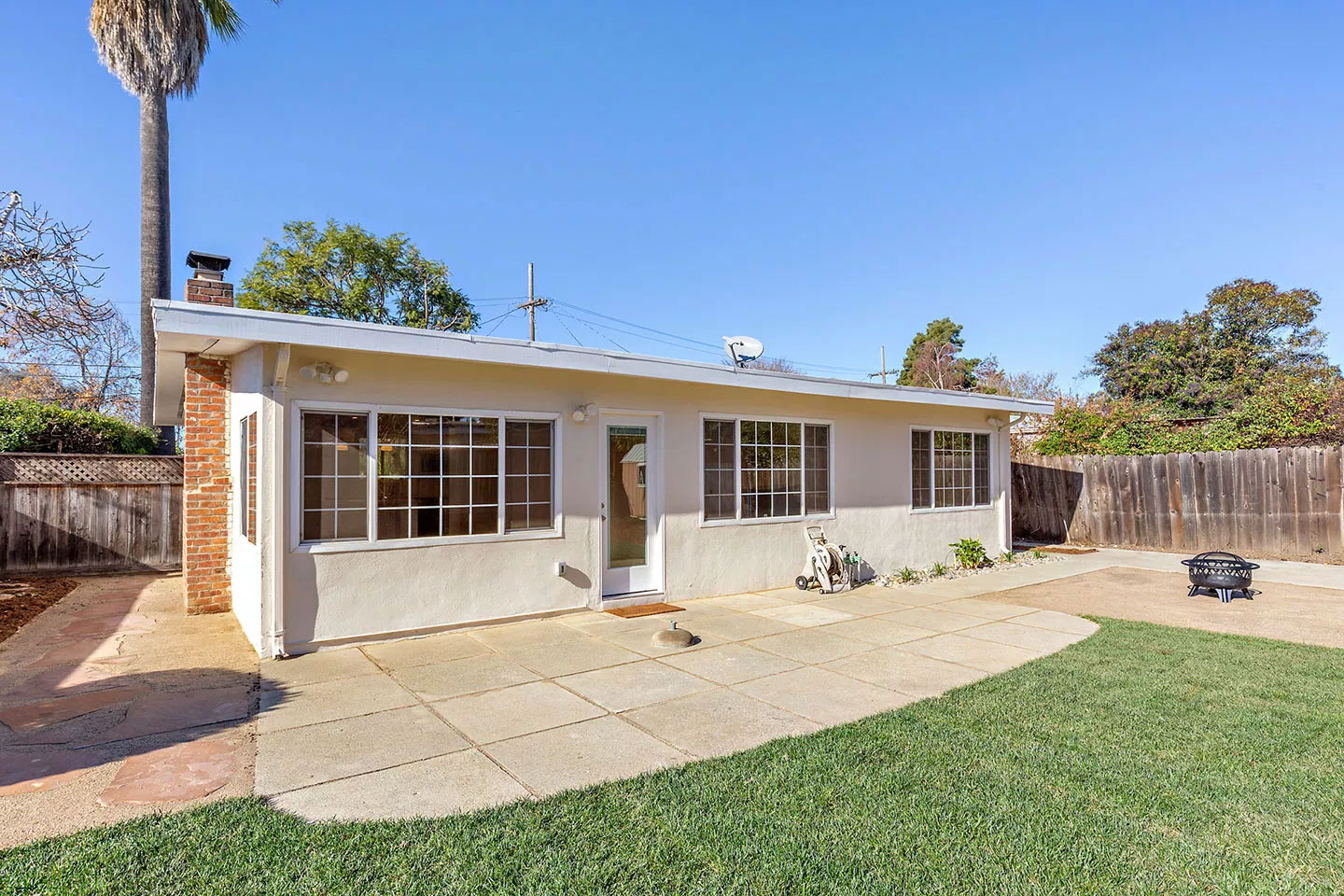 The image shows a single-story house with a white exterior, a garage door on the left, and a clear sky above.