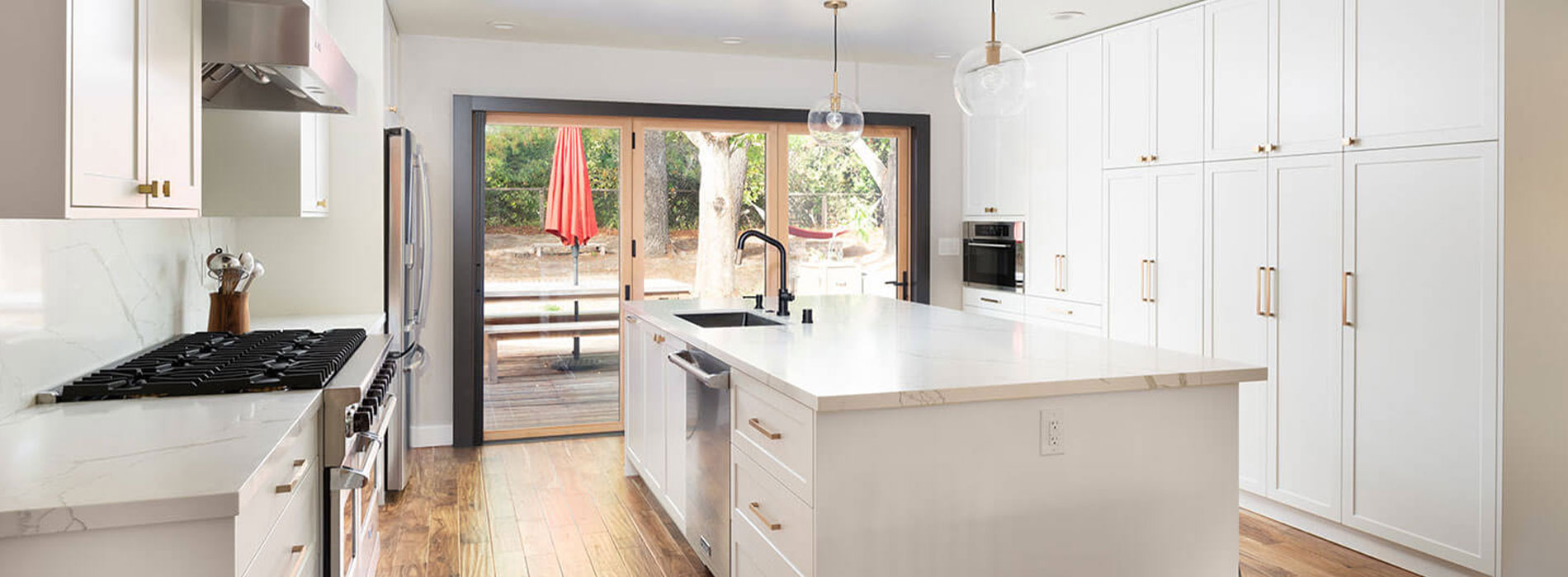 The image shows a modern kitchen interior with white cabinets, a marble countertop, stainless steel appliances, and a large island in the center.